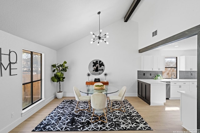 dining room featuring a notable chandelier, sink, light hardwood / wood-style flooring, and lofted ceiling with beams