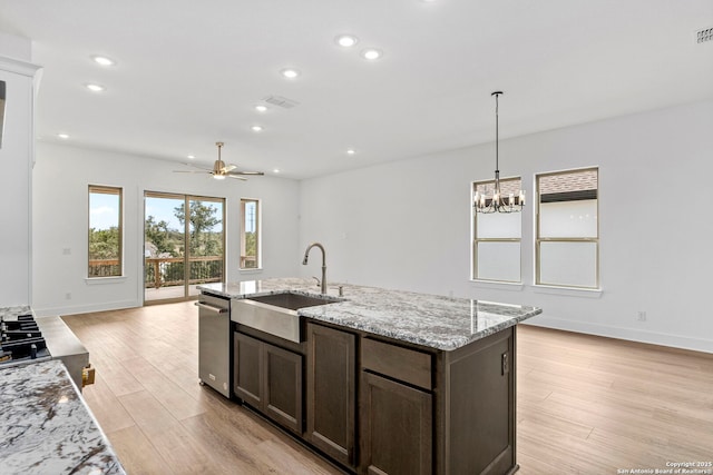 kitchen featuring dark brown cabinets, hanging light fixtures, light stone countertops, ceiling fan with notable chandelier, and sink