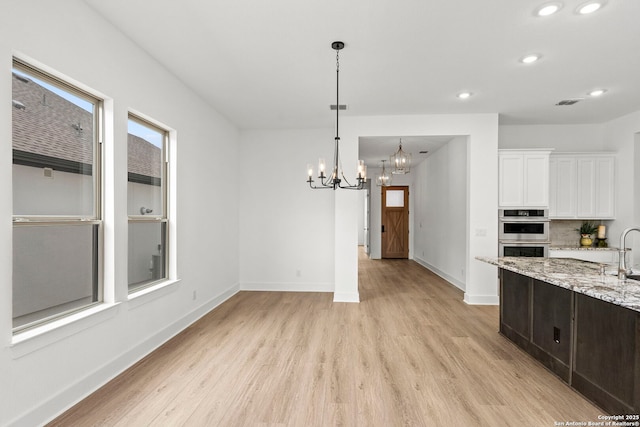 kitchen featuring white cabinetry, a chandelier, double oven, light hardwood / wood-style flooring, and light stone counters