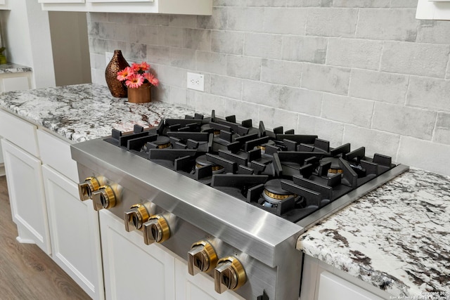 details with light stone countertops, white cabinets, stainless steel gas stovetop, and light hardwood / wood-style floors