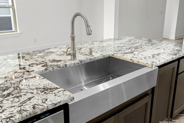 room details featuring sink, dark brown cabinets, and light stone countertops