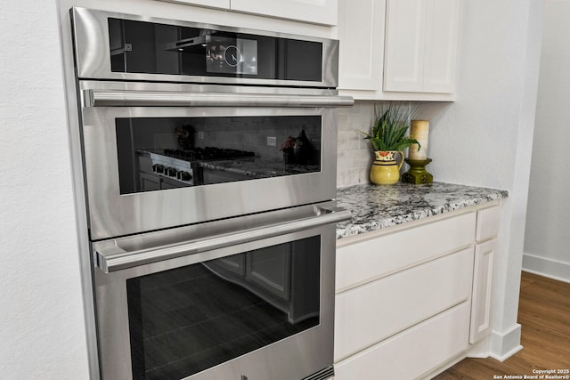 kitchen featuring dark wood-type flooring, white cabinets, light stone countertops, and stainless steel double oven