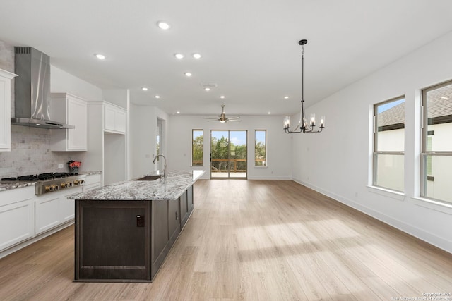 kitchen featuring decorative light fixtures, backsplash, wall chimney range hood, stainless steel gas cooktop, and ceiling fan with notable chandelier