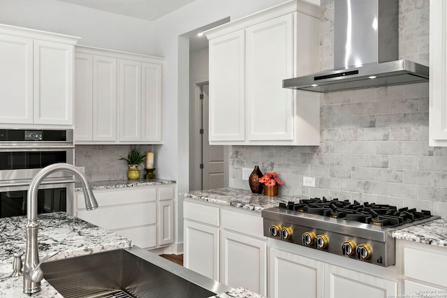 kitchen with wall chimney exhaust hood, sink, stainless steel appliances, and white cabinetry