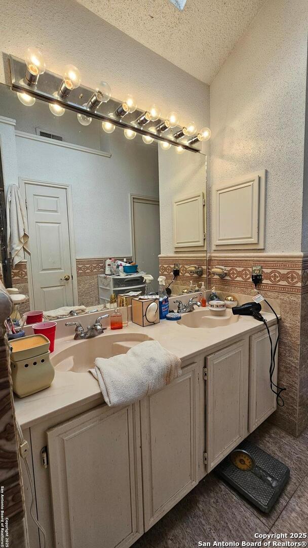 bathroom with a textured ceiling, double vanity, and wainscoting