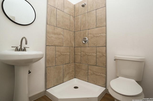 bathroom featuring toilet, hardwood / wood-style flooring, tiled shower, and sink