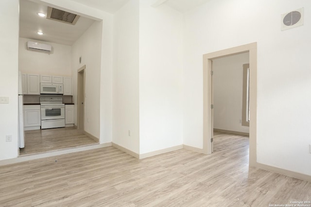 interior space featuring a wall unit AC, light hardwood / wood-style flooring, and a high ceiling