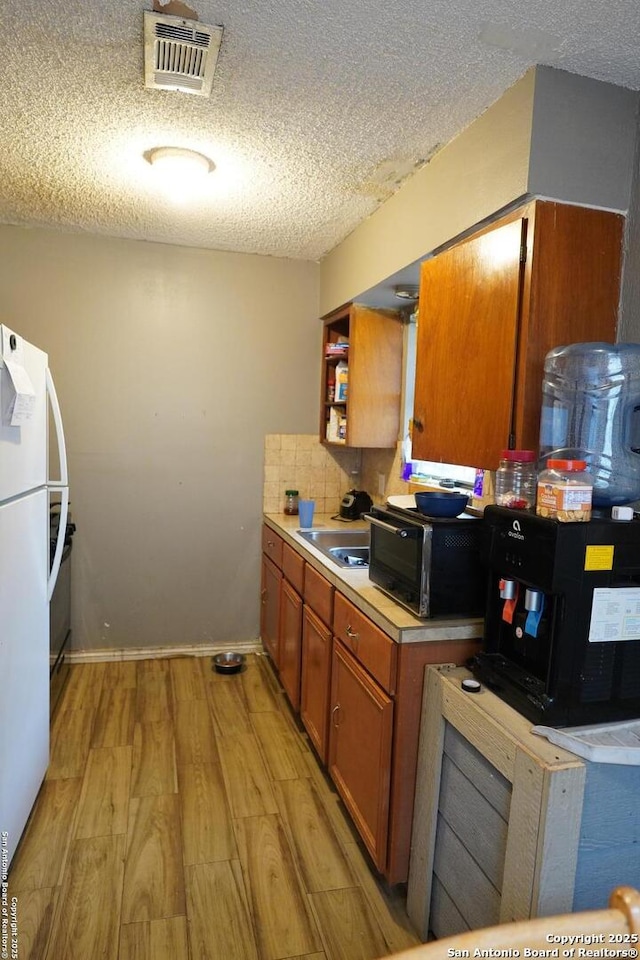 kitchen featuring backsplash, white fridge, sink, light wood-type flooring, and a textured ceiling