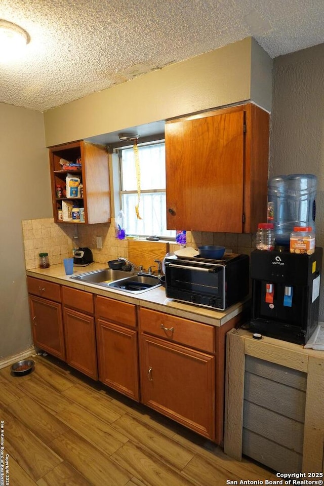 kitchen featuring decorative backsplash, sink, a textured ceiling, and light hardwood / wood-style flooring