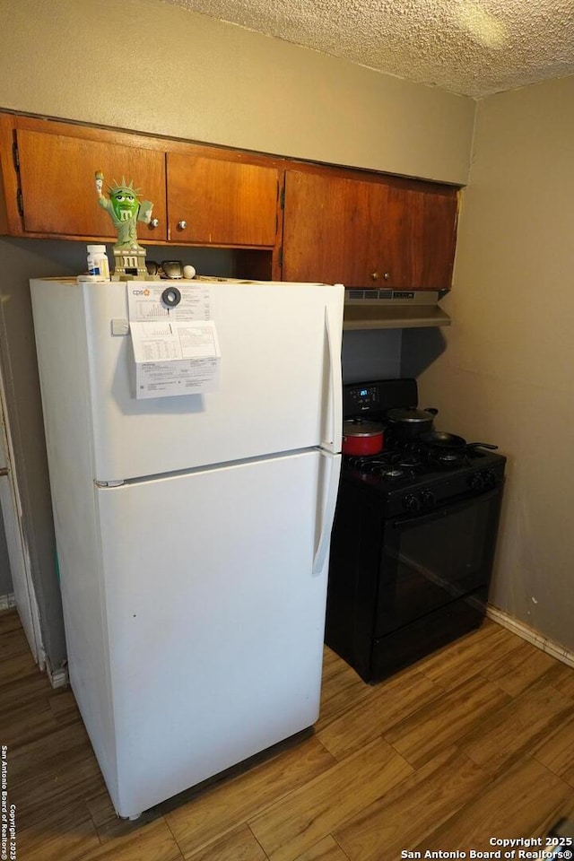 kitchen featuring white fridge, a textured ceiling, black gas range, and light hardwood / wood-style flooring