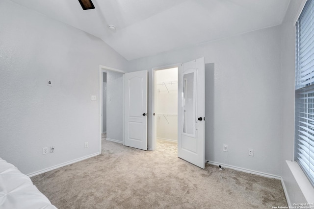 unfurnished bedroom featuring a spacious closet, light carpet, ceiling fan, a closet, and lofted ceiling