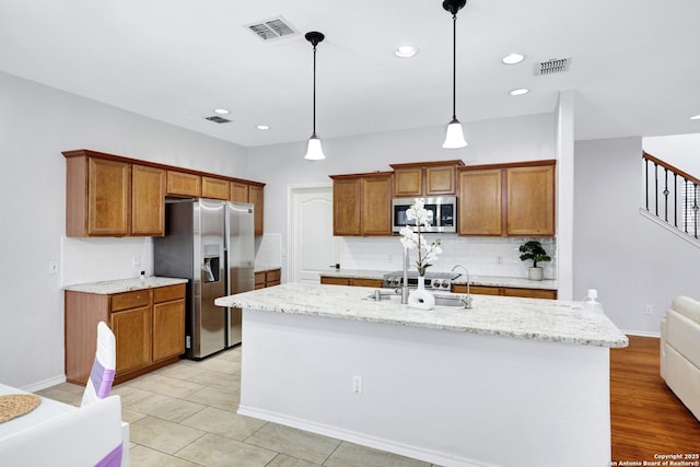 kitchen featuring a center island with sink, appliances with stainless steel finishes, tasteful backsplash, decorative light fixtures, and sink