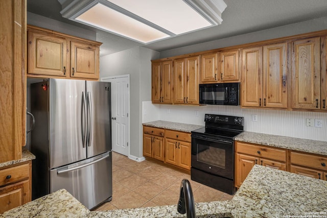 kitchen featuring light tile patterned floors, light stone counters, and black appliances