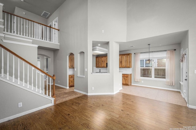 unfurnished living room with light wood-type flooring, a towering ceiling, and an inviting chandelier