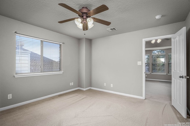 spare room featuring ceiling fan, light colored carpet, and a textured ceiling