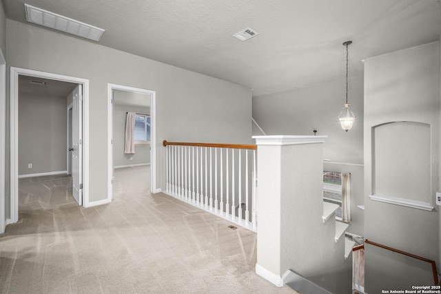 hallway with light colored carpet, a textured ceiling, and a healthy amount of sunlight