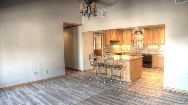 kitchen featuring black dishwasher, a high ceiling, a kitchen breakfast bar, a kitchen island, and light hardwood / wood-style flooring