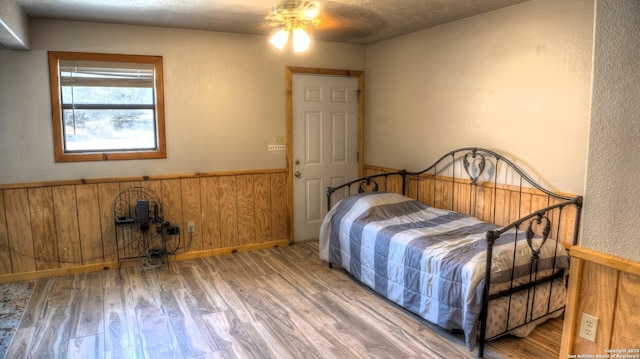 unfurnished bedroom featuring ceiling fan, hardwood / wood-style floors, a textured ceiling, and wooden walls