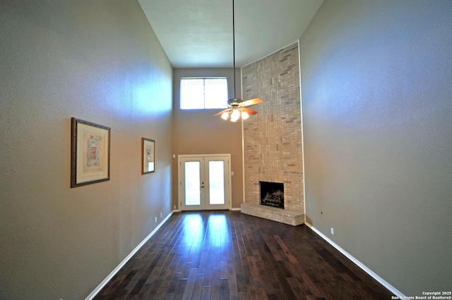 unfurnished living room with ceiling fan, a fireplace, a towering ceiling, dark wood-type flooring, and french doors