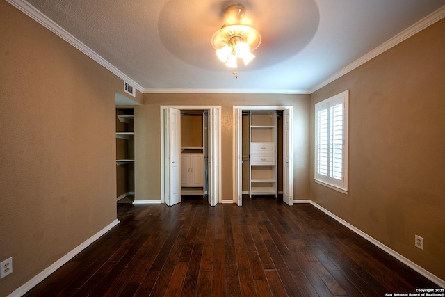 unfurnished bedroom with ceiling fan, two closets, dark hardwood / wood-style flooring, and crown molding