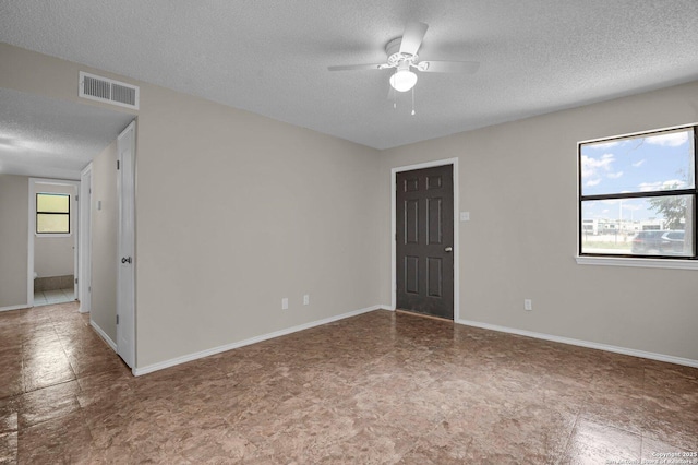 empty room featuring ceiling fan, plenty of natural light, and a textured ceiling