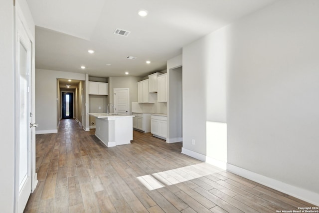 kitchen with sink, white cabinets, light hardwood / wood-style flooring, and an island with sink