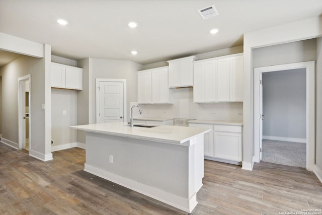 kitchen with light hardwood / wood-style floors, sink, white cabinets, and a center island with sink