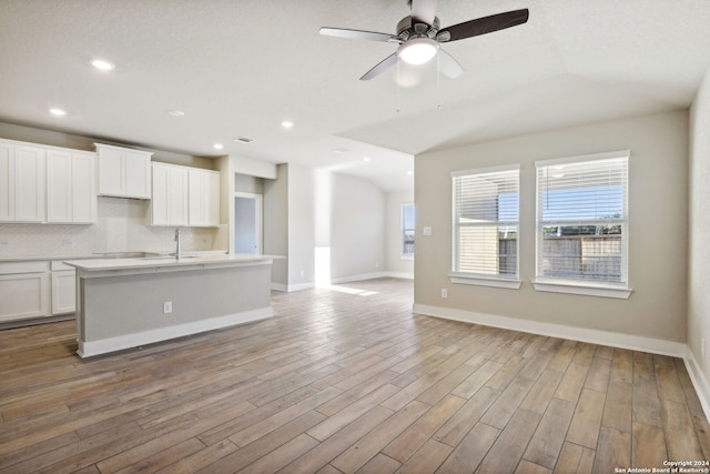 kitchen featuring white cabinetry, light hardwood / wood-style floors, a center island with sink, ceiling fan, and backsplash