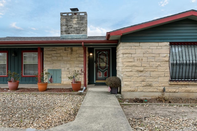 doorway to property featuring stone siding, a chimney, a porch, and roof with shingles