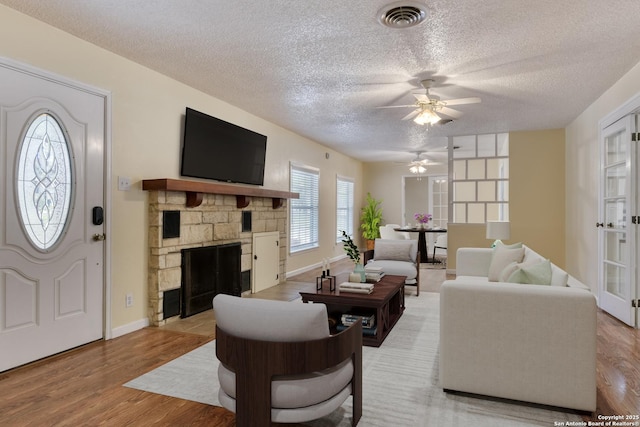 living room with light wood finished floors, visible vents, a textured ceiling, and a stone fireplace