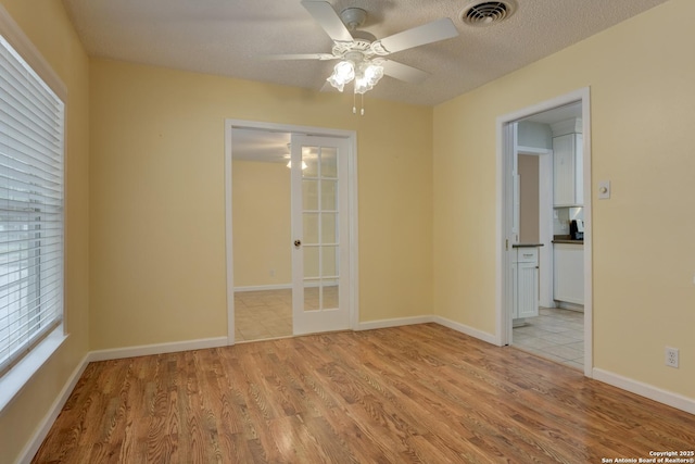 unfurnished room with light wood finished floors, visible vents, baseboards, a ceiling fan, and a textured ceiling