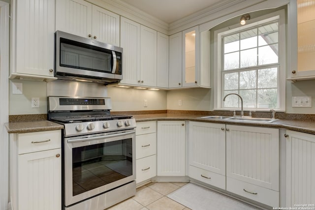 kitchen with light tile patterned floors, a sink, appliances with stainless steel finishes, dark countertops, and glass insert cabinets