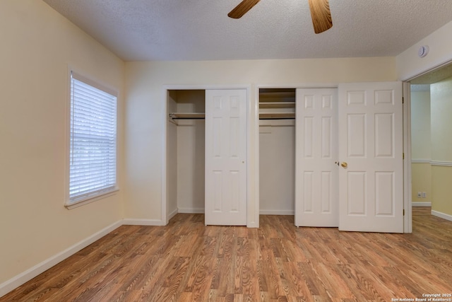 unfurnished bedroom with a textured ceiling, ceiling fan, wood finished floors, baseboards, and multiple closets