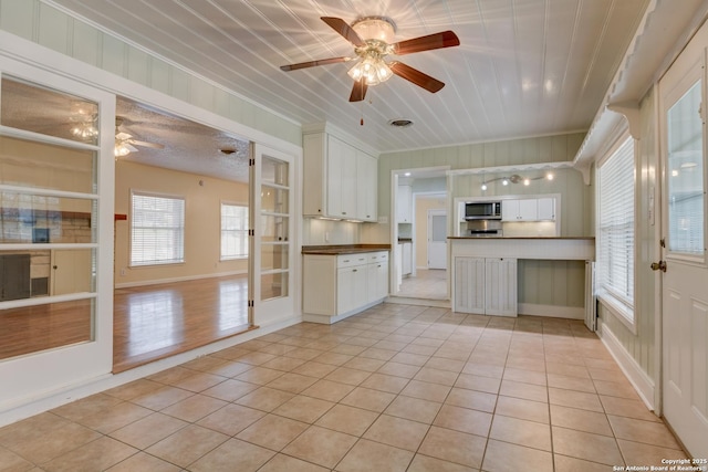 kitchen with light tile patterned floors, a ceiling fan, white cabinets, stainless steel microwave, and dark countertops