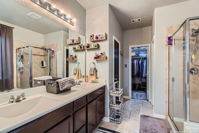 bathroom with a textured ceiling, a shower with door, tile patterned floors, and vanity