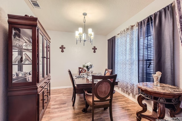 dining space with light wood-type flooring, a chandelier, and a textured ceiling