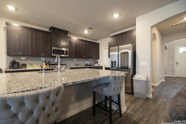 kitchen featuring a kitchen bar, light stone countertops, stainless steel appliances, and dark brown cabinets