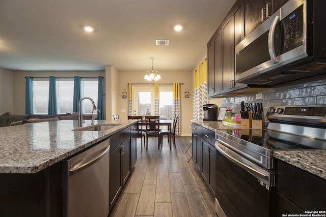 kitchen with light stone countertops, stainless steel appliances, an island with sink, decorative backsplash, and sink