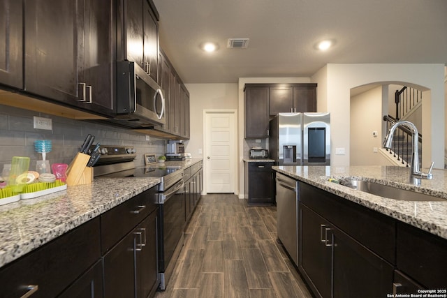 kitchen featuring appliances with stainless steel finishes, tasteful backsplash, sink, light stone counters, and dark brown cabinets