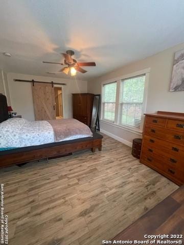 bedroom featuring hardwood / wood-style flooring, ceiling fan, and a barn door