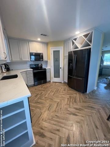 kitchen featuring electric stove, light parquet flooring, sink, white cabinetry, and black refrigerator