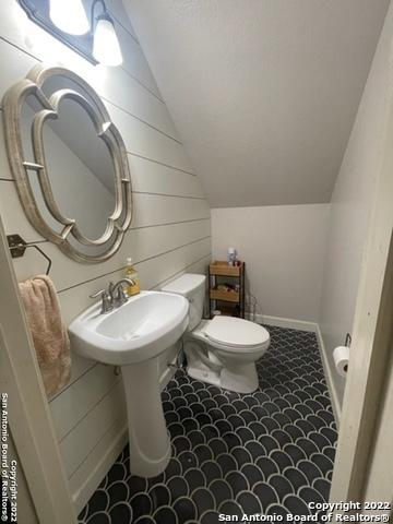 bathroom with vaulted ceiling, toilet, and wooden walls