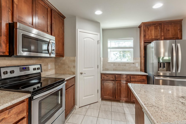 kitchen featuring light tile patterned floors, decorative backsplash, appliances with stainless steel finishes, and light stone counters