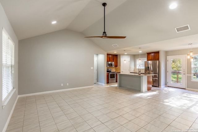 kitchen with light stone countertops, appliances with stainless steel finishes, decorative light fixtures, an island with sink, and vaulted ceiling