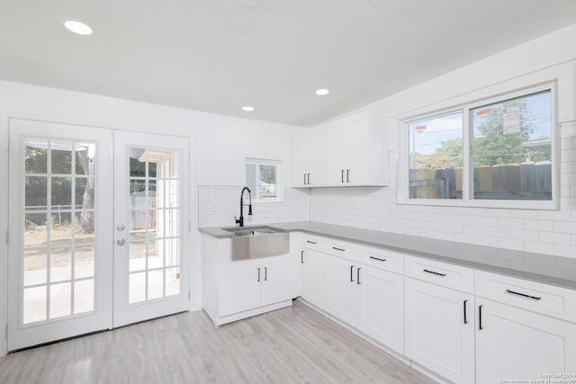 kitchen with decorative backsplash, plenty of natural light, white cabinets, light hardwood / wood-style flooring, and sink