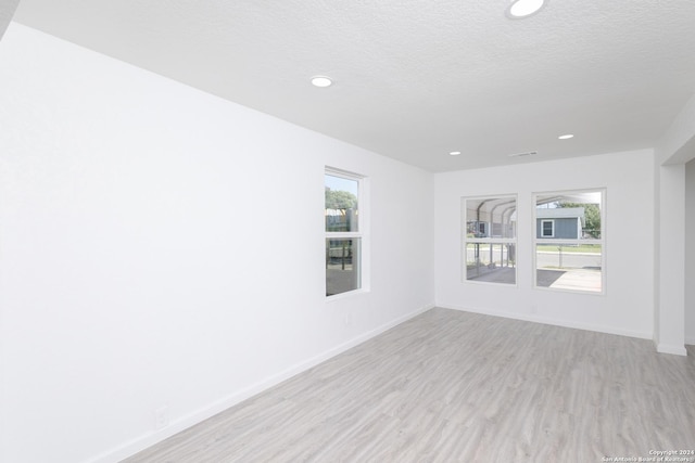 spare room featuring a textured ceiling, light hardwood / wood-style floors, and plenty of natural light