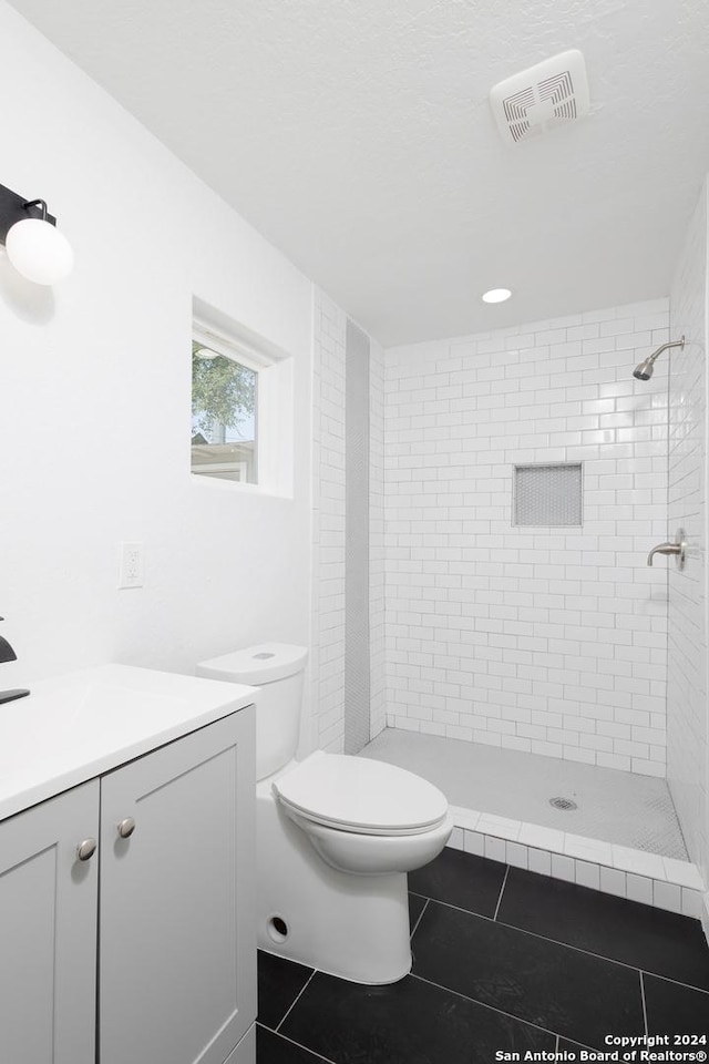 bathroom with tile patterned floors, toilet, tiled shower, and vanity