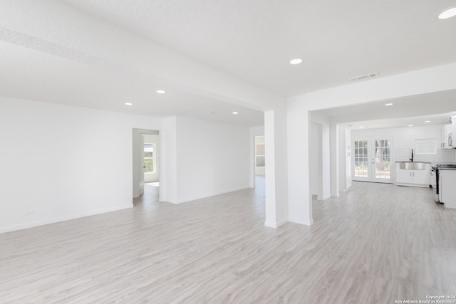 unfurnished room with french doors, sink, a textured ceiling, and light hardwood / wood-style floors