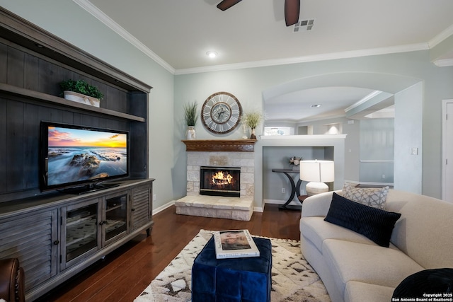 living room with crown molding, a stone fireplace, built in features, and dark hardwood / wood-style floors