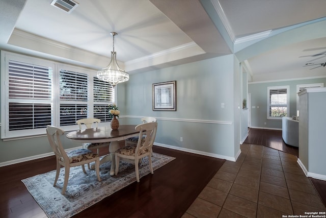 dining space with a raised ceiling, crown molding, ceiling fan with notable chandelier, and dark tile patterned flooring